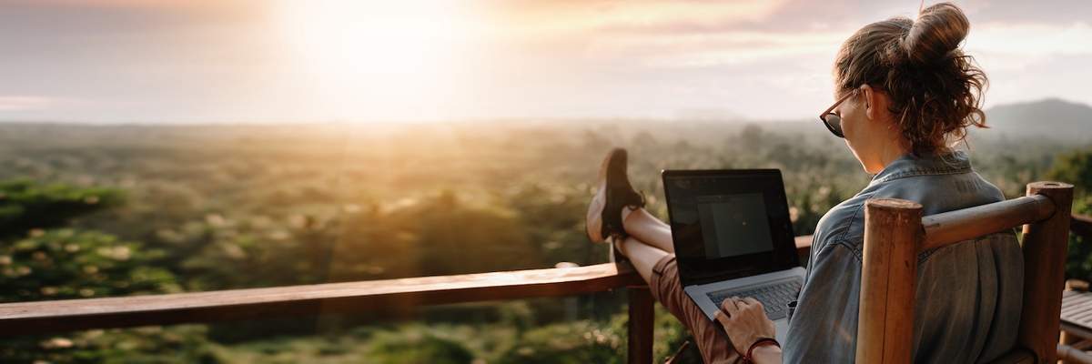 Young business woman working at the computer in cafe on the rock. Young girl downshifter working at a laptop at sunset or sunrise on the top of the mountain to the sea, working day.